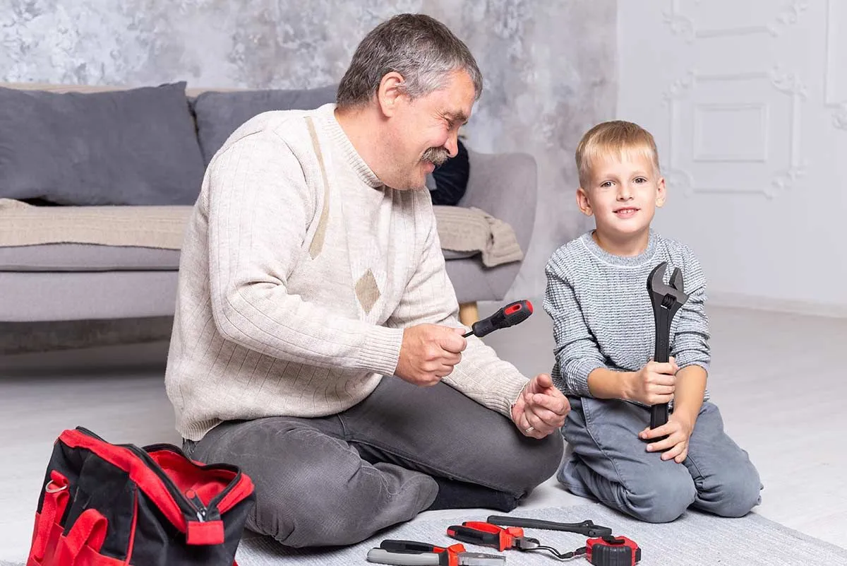 Grandpa and grandson sat on the floor with screwdrivers to make a toy robot.
