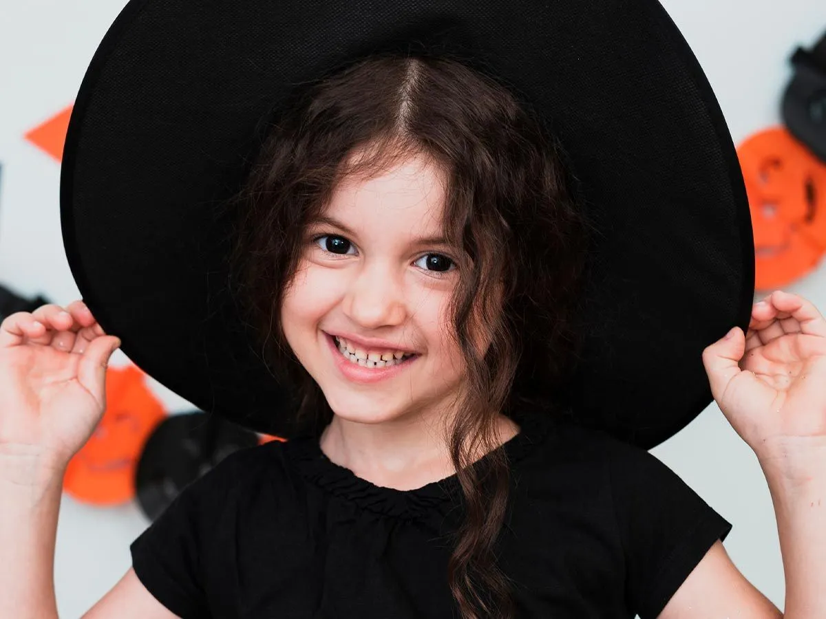 Little girl wearing a large black witch's hat smiling.