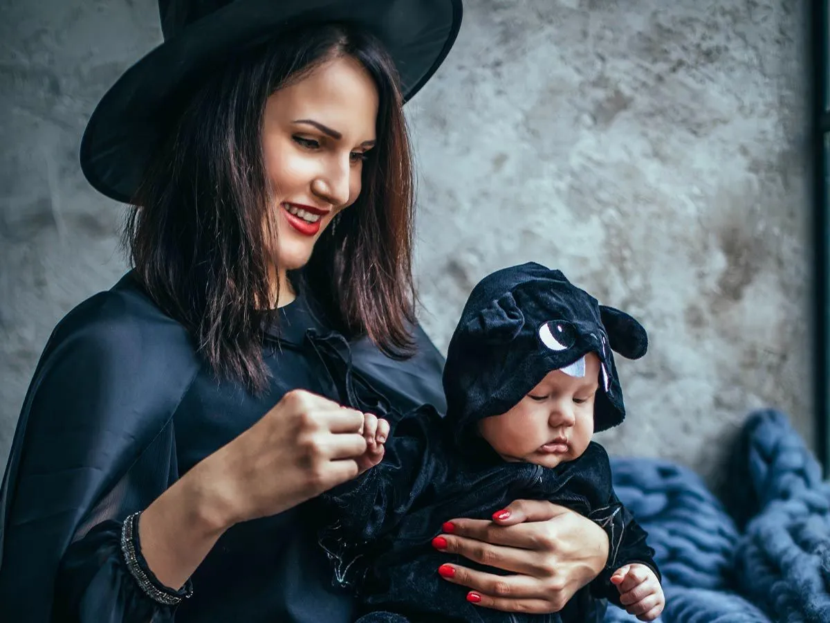 Mum dressed as a witch holding her baby girl dressed as a bat.