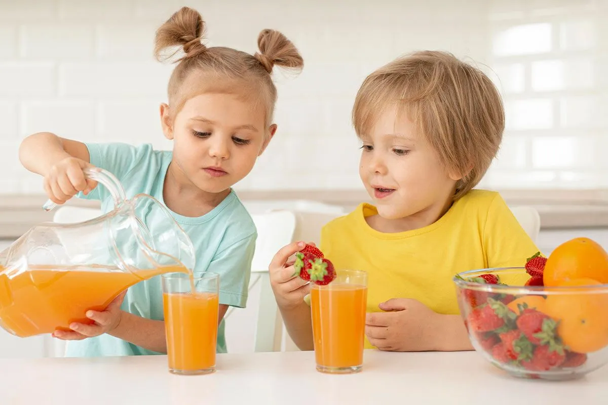 Young girl and boy in the kitchen, the girl is pouring a glass of orange juice for herself and her brother.