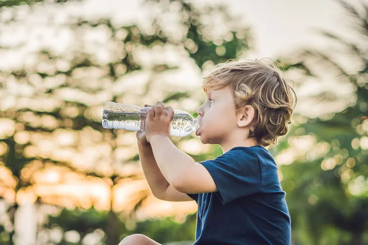 Young boy sat drinking water from a bottle in the garden.