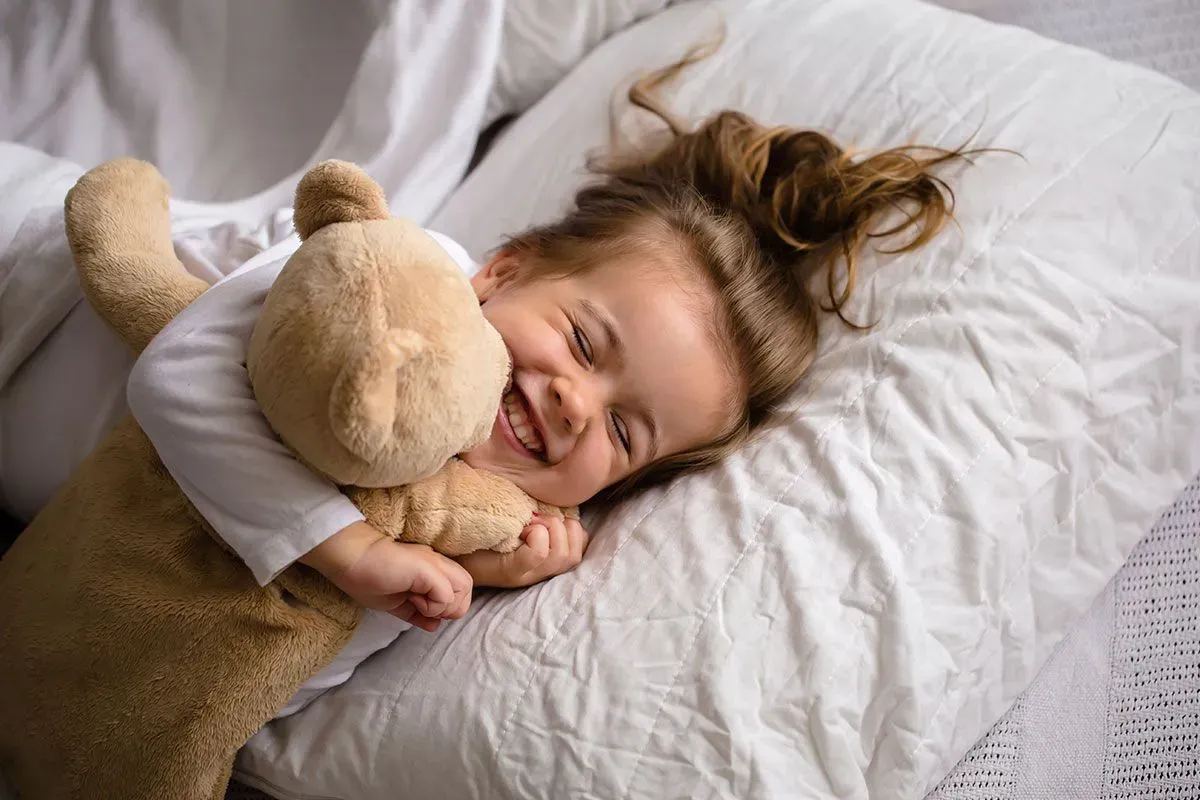Little girl lying in bed smiling and cuddling her teddy bear.