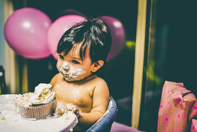 Baby boy in a high chair sat with a piece of cake in front of him and icing on his face.