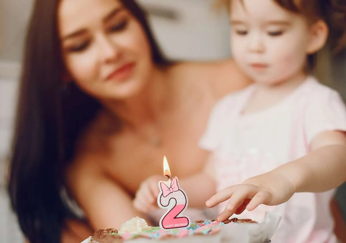 Mum holding her two year old daughter who has a birthday cake in front of her.