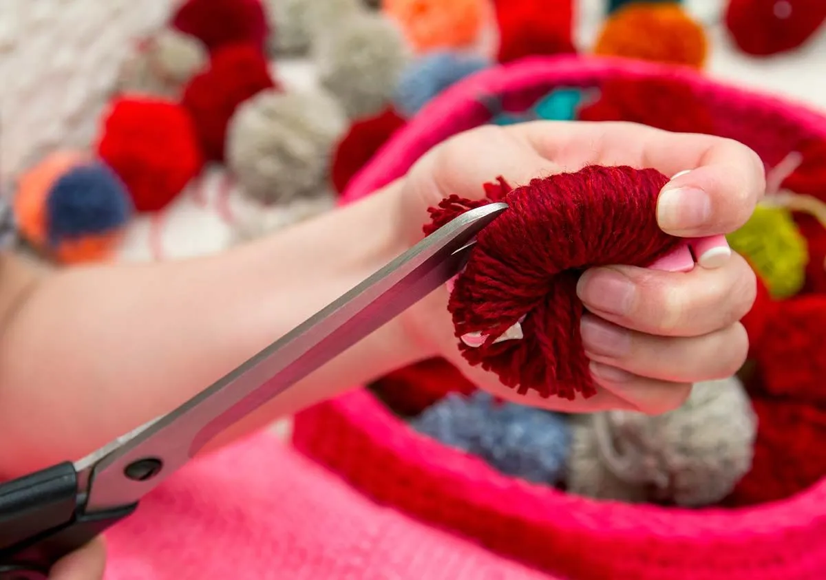Close up of a hand cutting string with scissors to make a pom pom Gruffalo model.