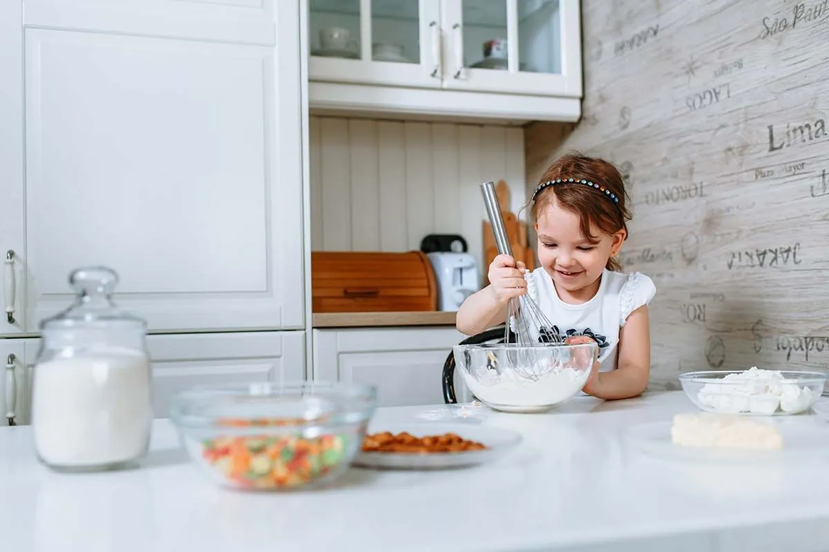 A little girl smiles as she whisks the lion cake mixture in a bowl.