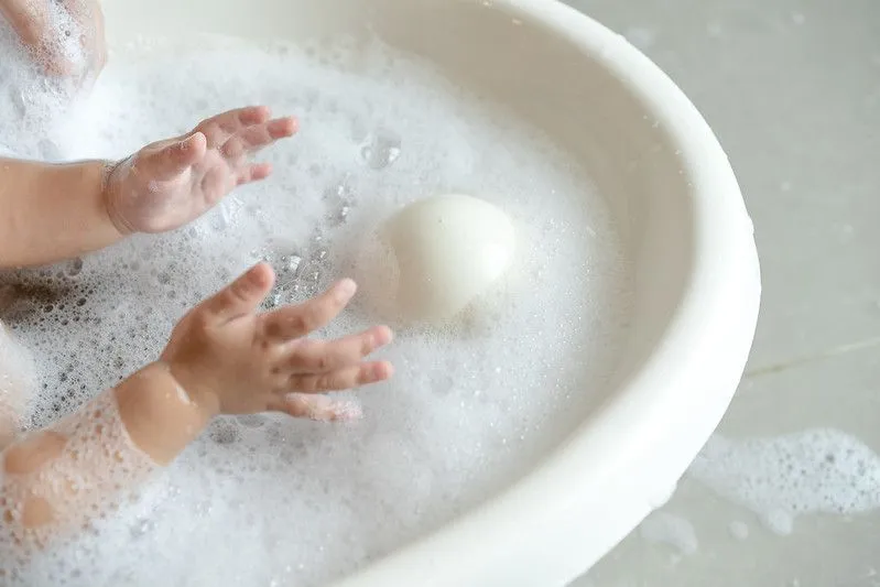 Close up of a young child in the bath tube reaching for a ball of soap.