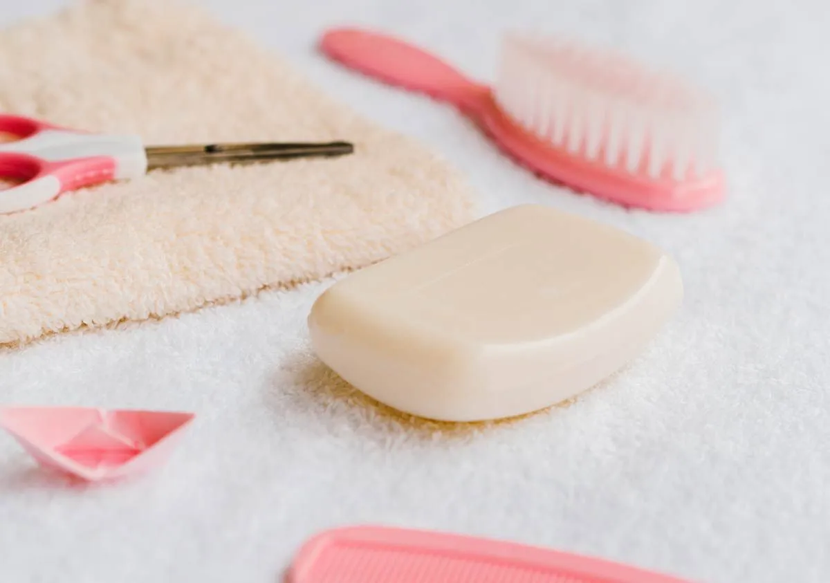 A bar of soap for kids lying on a towel, with a pink hairbrush and some scissors next to it.