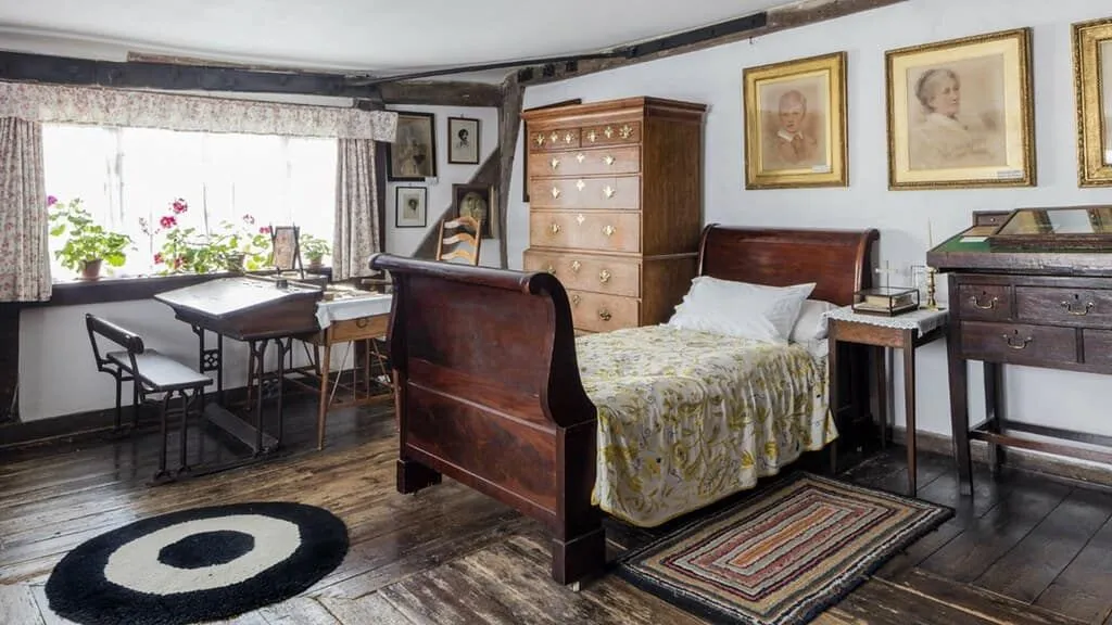 A modest Victorian bedroom with wooden furnishings and some pictures on the wall.o