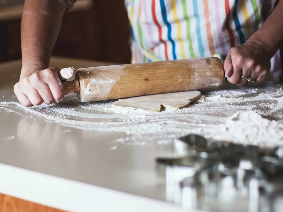 Close up of a large rolling pin being used by someone in a stripey rainbow coloured apron to roll out icing to make a pug cake.