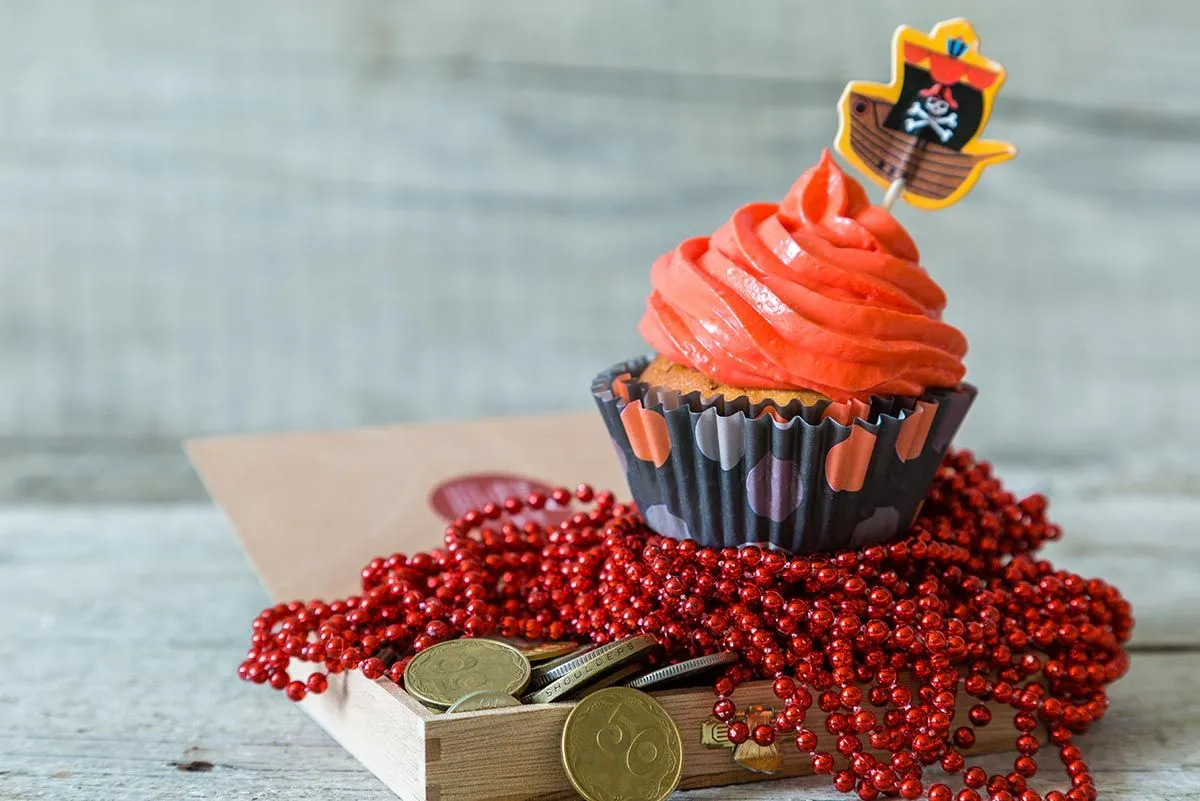 A pirate-themed cupcake: cupcake with orange icing and a pirate ship decoration sitting on an open treasure chest.