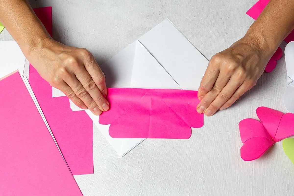 Hands folding down pink paper to make an origami flamingo.