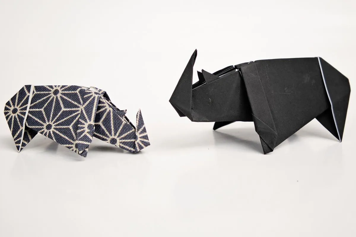 Two origami rhinos standing up facing each other as if in the wild.