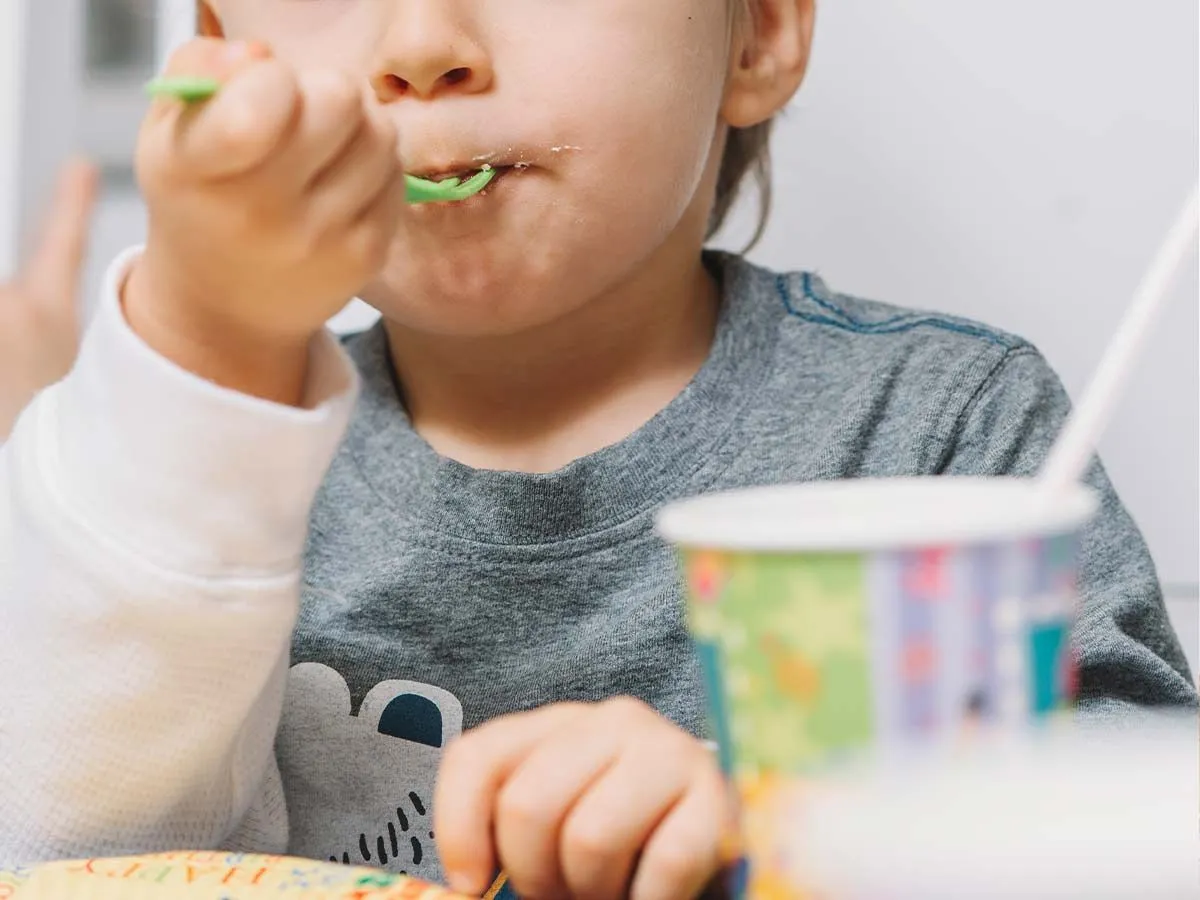 Close up of young boy eating a bite of Toy Story cake on a green plastic fork.