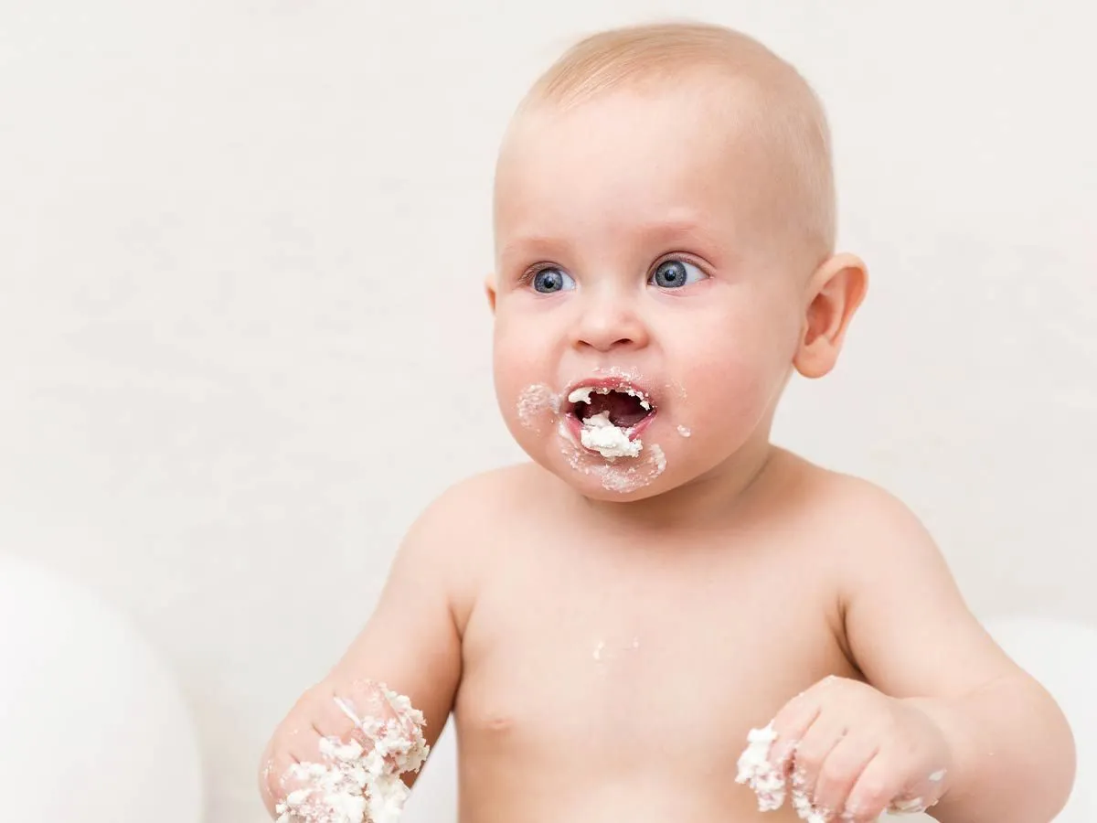 Cute baby with a messy mouth and hands after enjoying a taste of ladybird cake.
