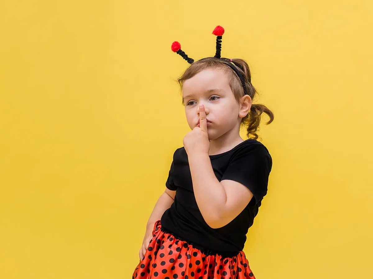 Little girl dressed as a ladybird poses for the camera against a yellow background.