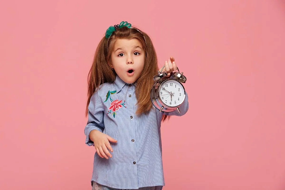 Little girl holding up a clock, learning to tell time.