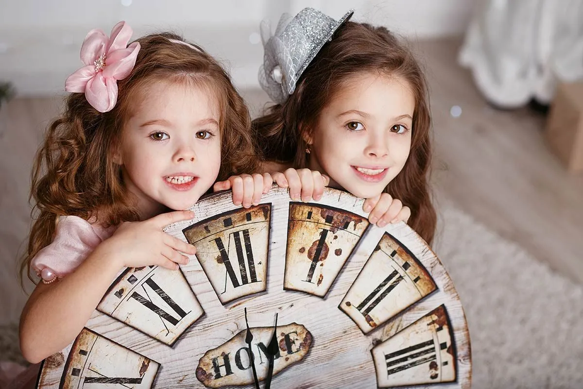 Two sisters crouching behind a large clock smiling.