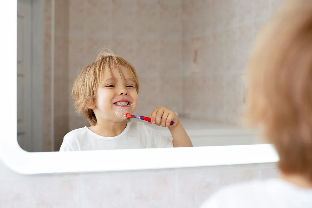A little boy grins into the mirror as her brushes his teeth, he is happily earning points for his reward chart.
