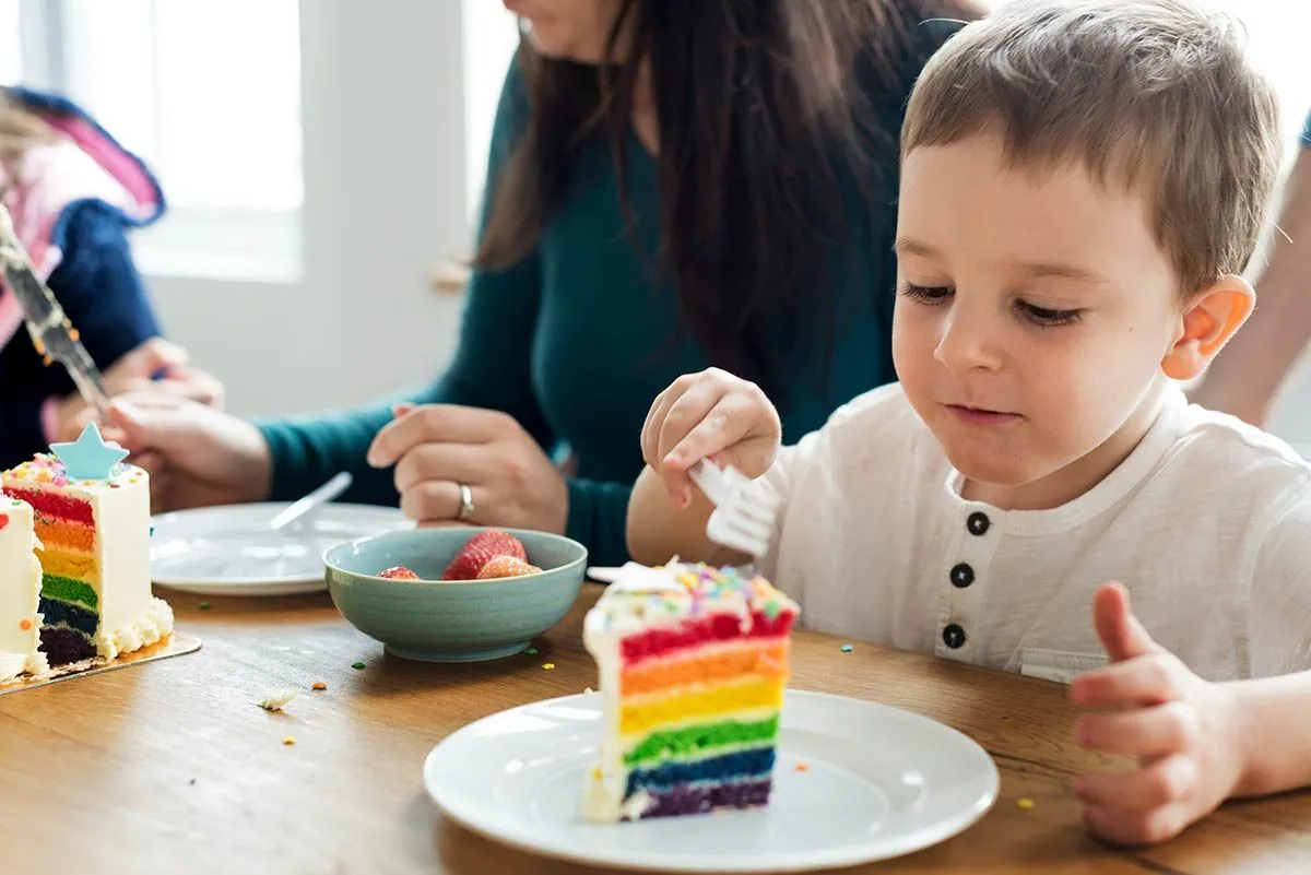Young boy eating a slice of rainbow Power Ranger cake.