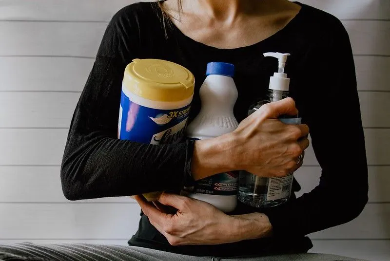 A close up image of a woman holding three different cleaning products to try and remove biro from leather.