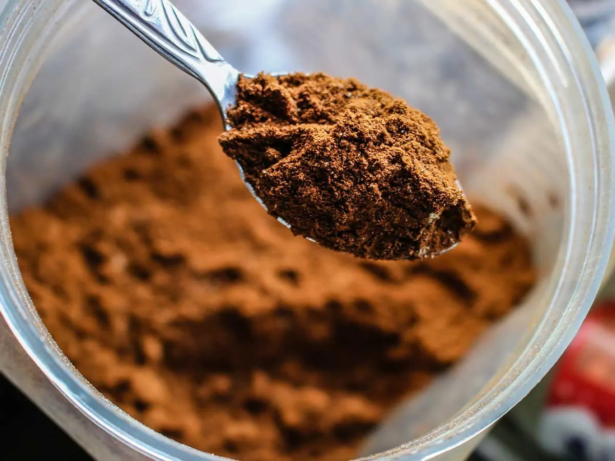 A close up image of a teaspoon of cocoa powder, an ingredient in this digger cake recipe.