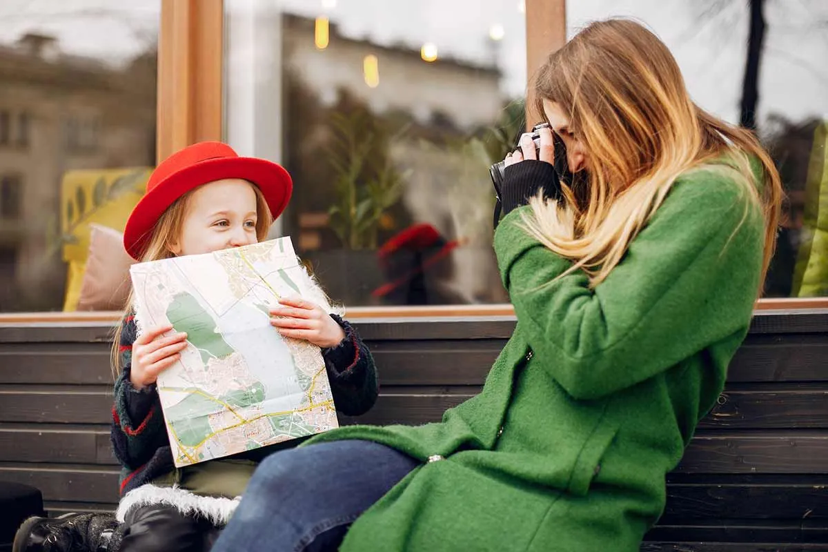 Mum sat on a bench taking a photo of her daughter who is holding a map.