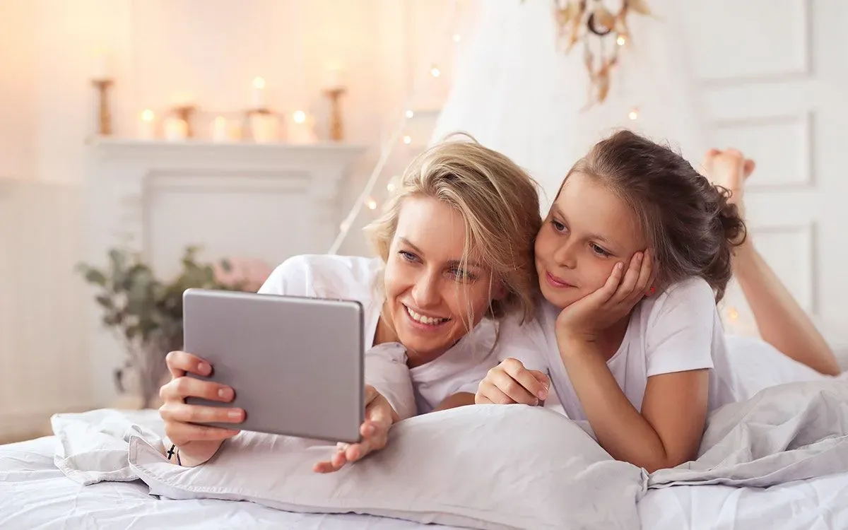 A mother and daughter are lying next to each other looking at an iPad, learning about the present perfect tense.
