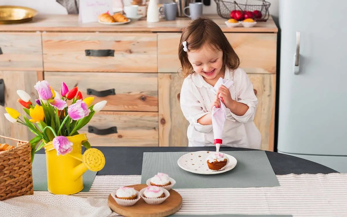 A young girl smiles as she uses a piping bag to ice some cupcakes.