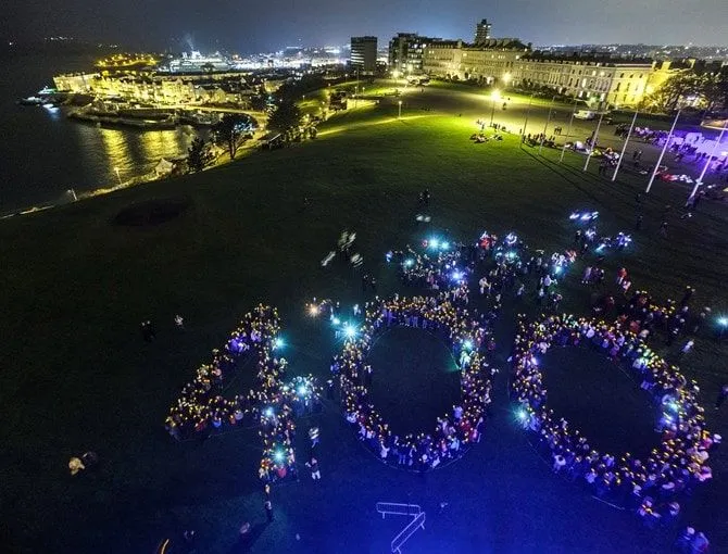 People stood in the shape of the number 400 lit up at night.