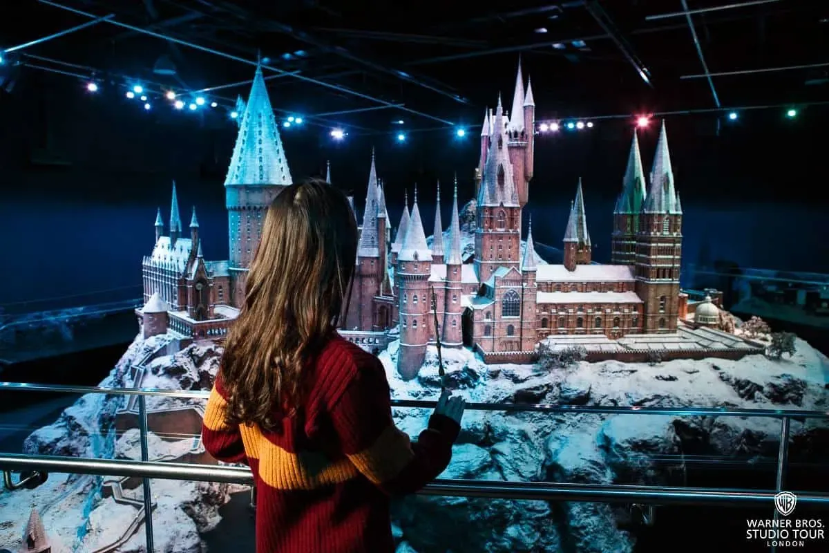 Young girl, dressed in a Gryffindor jumper and holding a wand, looking at the Hogwarts model at the studio tour.