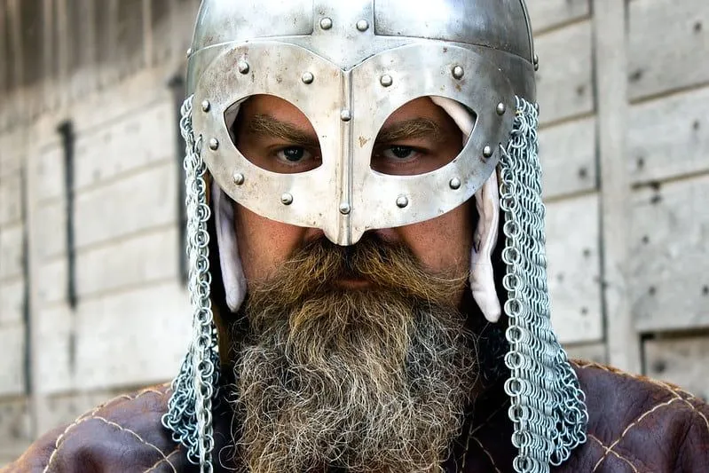 A Viking man wearing a Viking helmet looks straight at the camera.