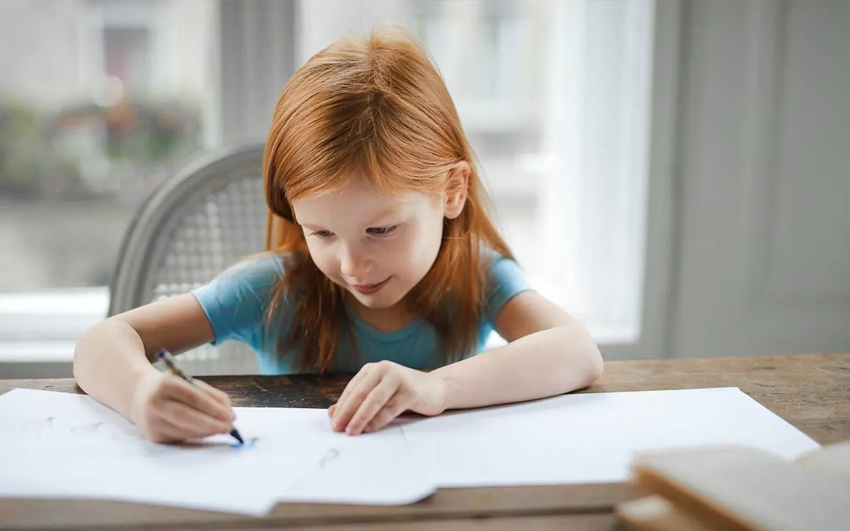 Young girl sat at a table writing about Stone Age tools in her workbook.
