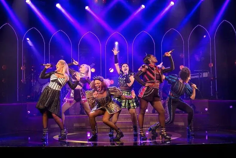 The cast of Six performing a dramatic musical number on stage with purple neon lights.