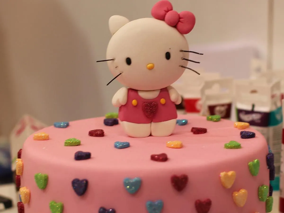 Pink birthday cake with sparkly heart sprinkles and a fondant icing Hello Kitty figure on top.