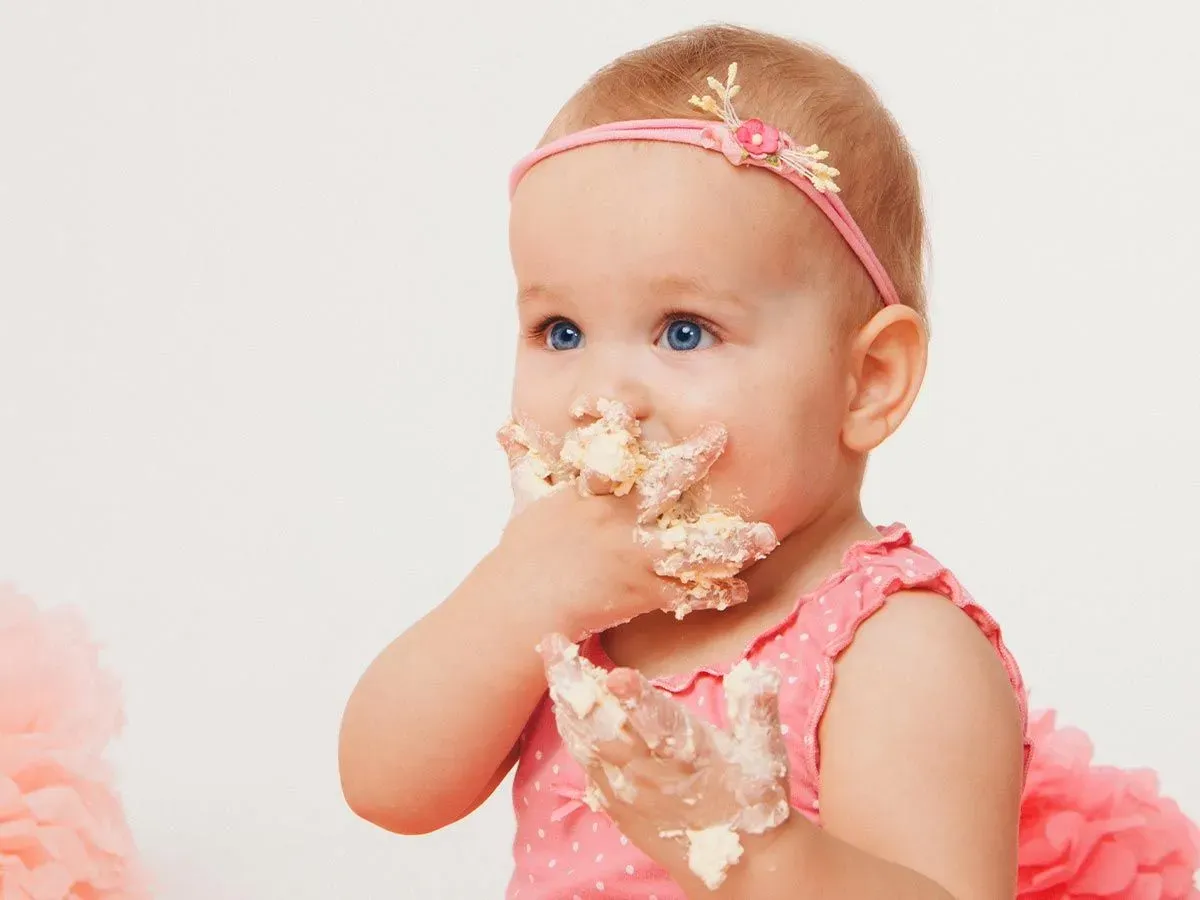 Toddler dressed in a pink outfit eating cake with her hands.