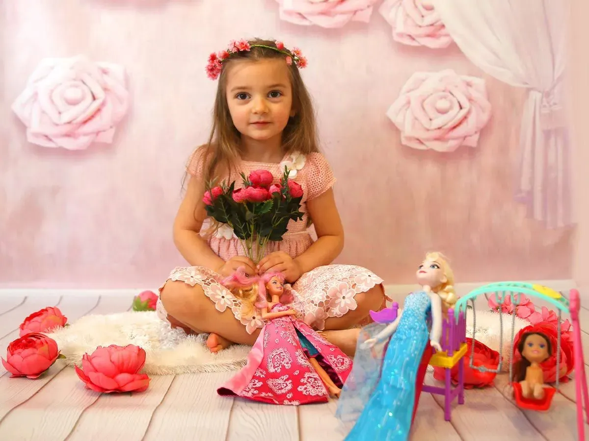 Little girl dressed as a pink princess, sat on the floor in a pink room with her Barbie dolls.