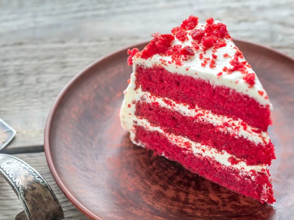 Slice of red velvet cake with white frosting and cake crumb on top.