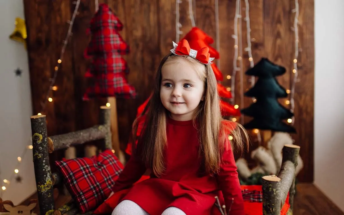 Little girl sat on a seat with Christmas decorations behind, thinking about the answers to Christmas riddles.