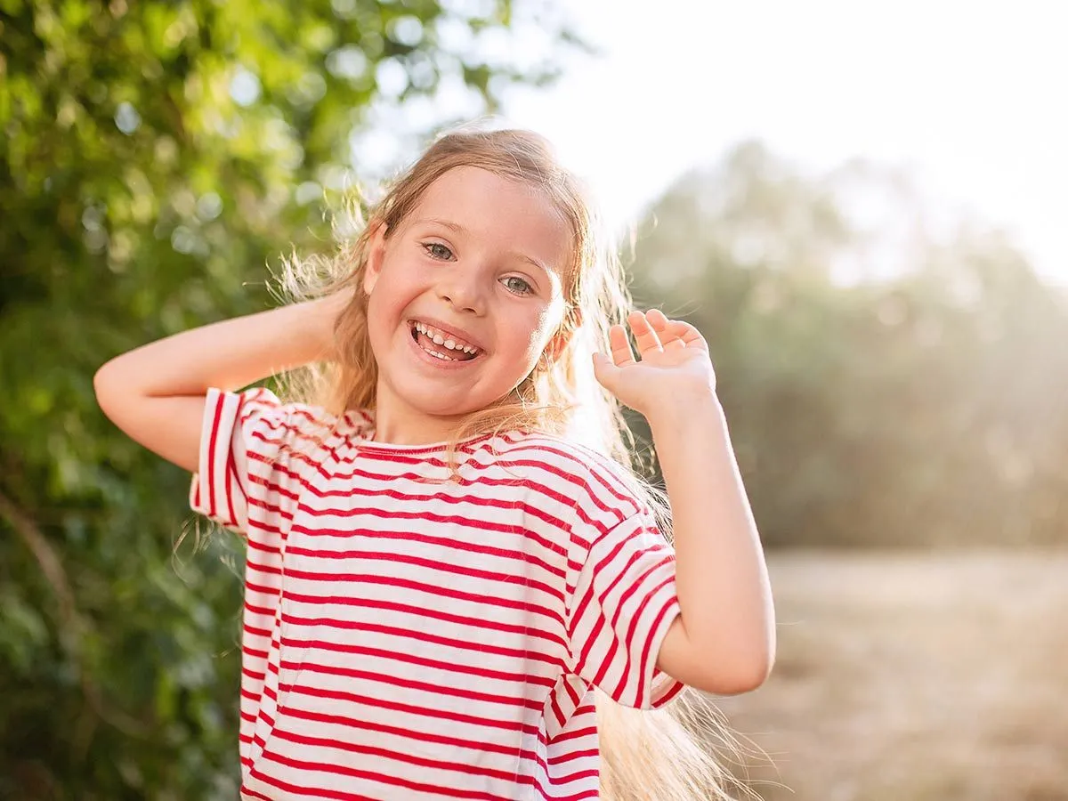 Girl wearing striped red and white top standing in the garden in the sun smiling at summer puns.