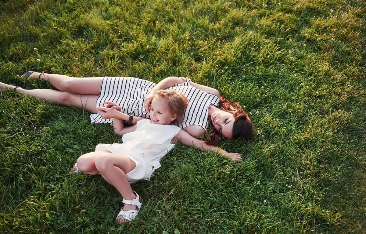 Mum and daughter lying in the grass smiling at summer puns.