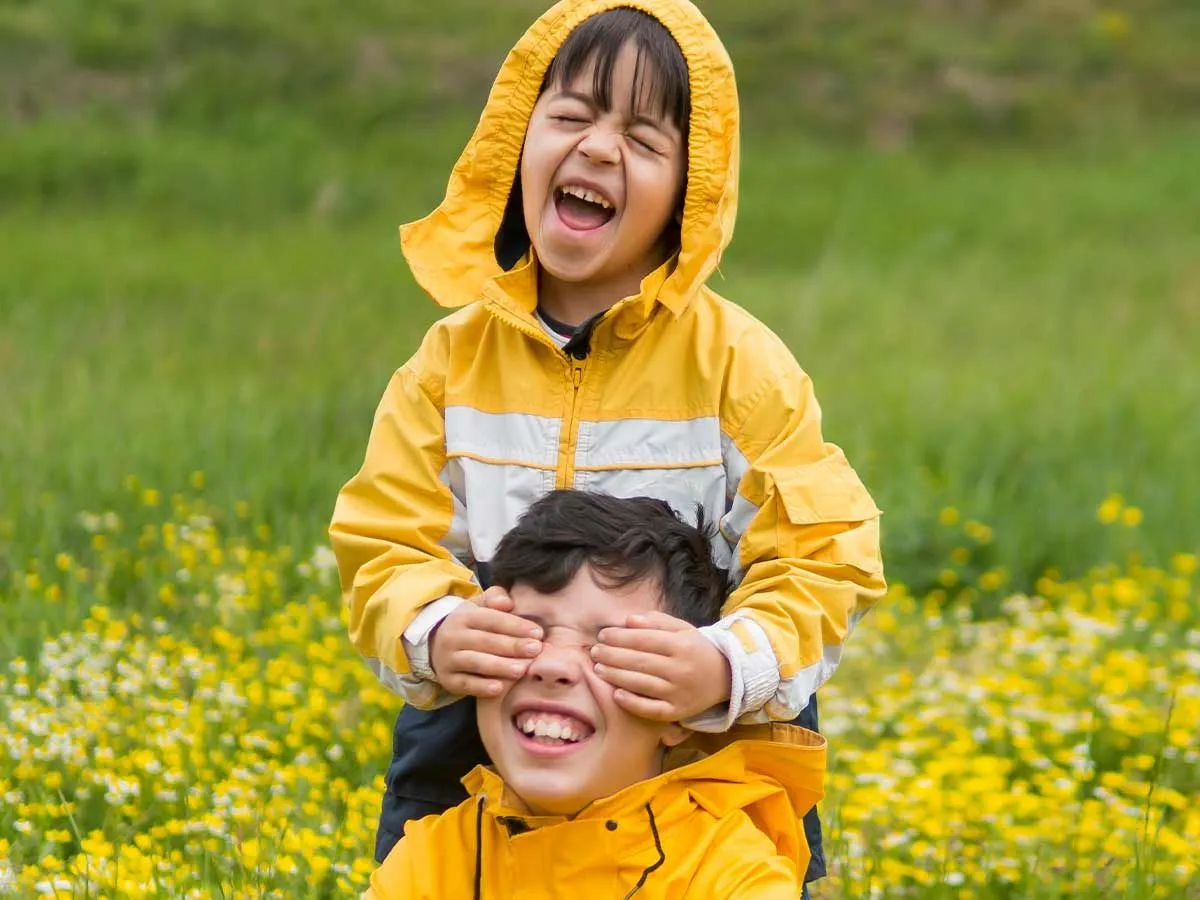 Two siblings wearing matching raincoats laughing in the garden together at summer puns.