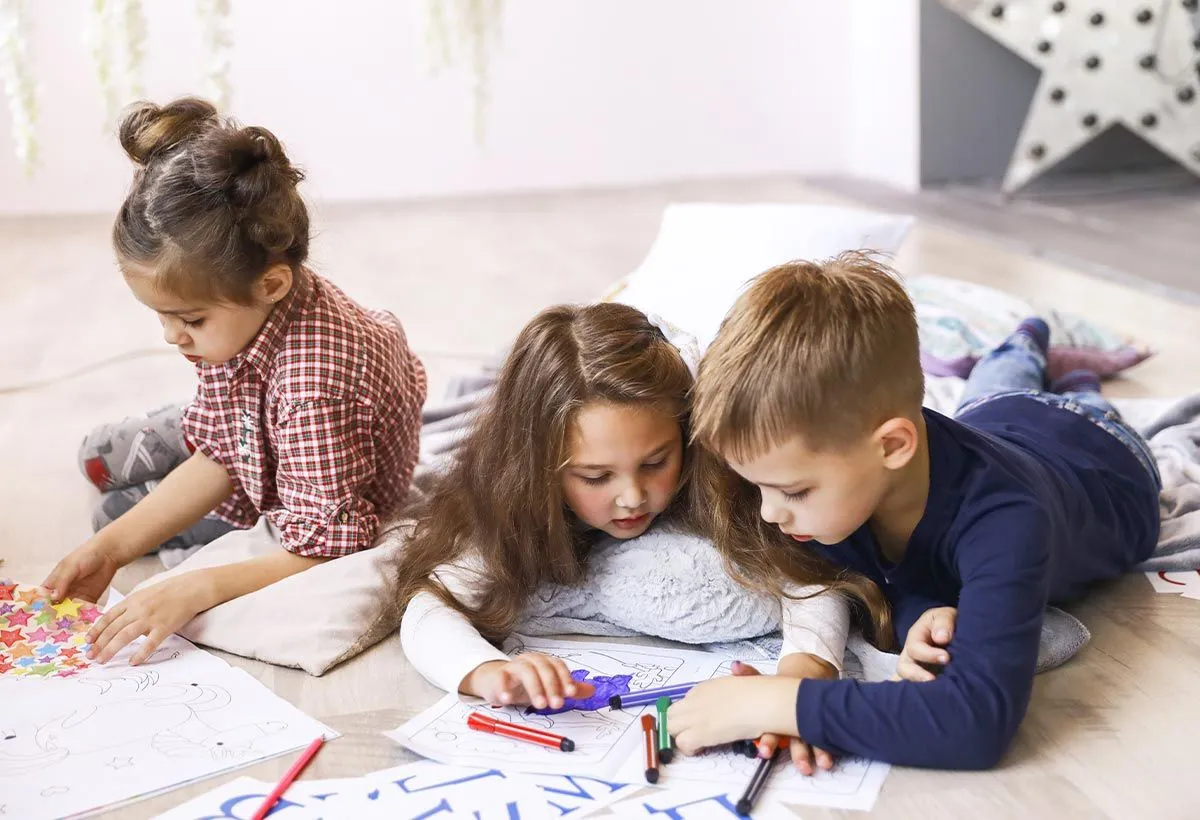 Three young kids lying on the floor drawing on paper to help learn about the passive voice.