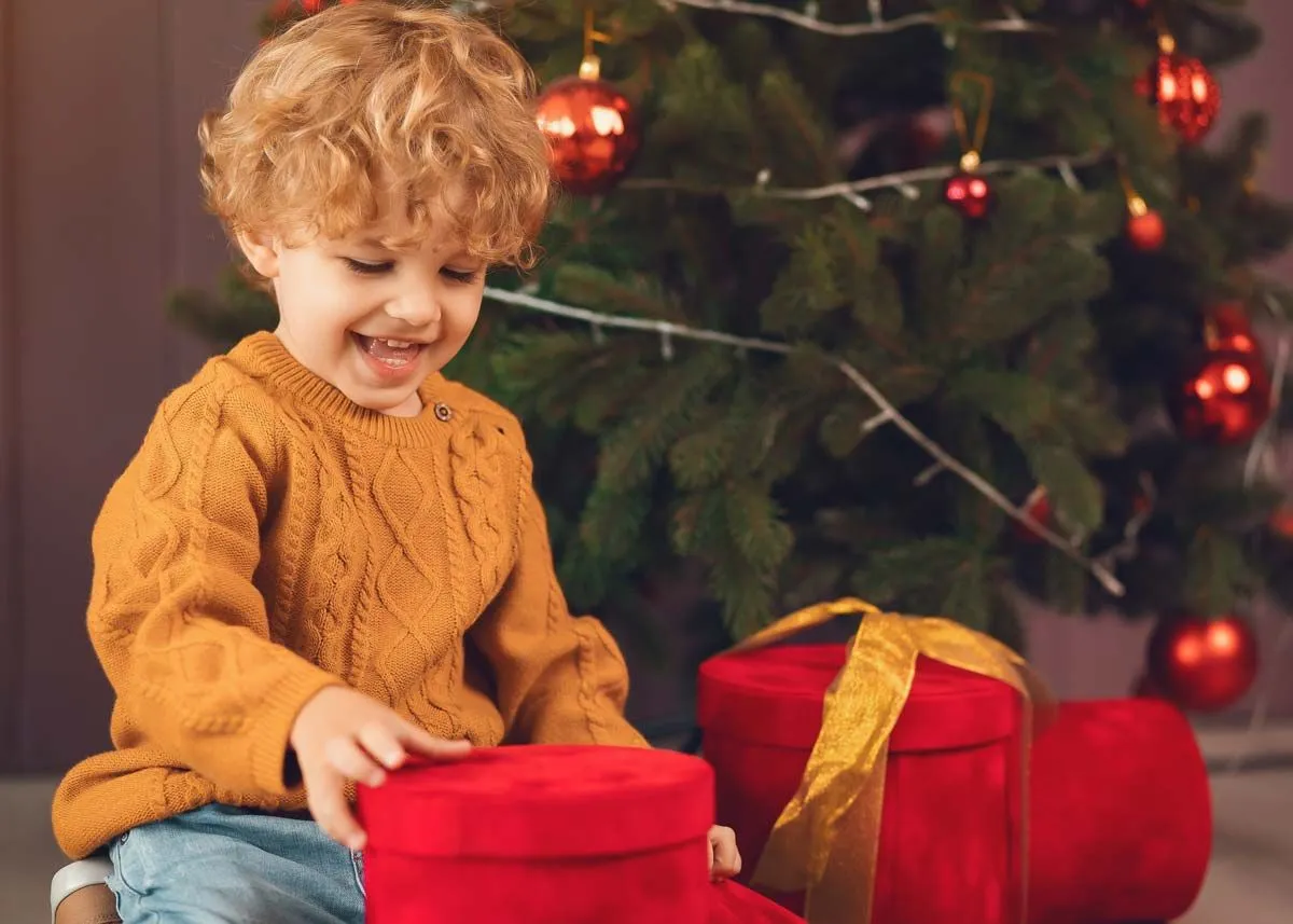 Little boy sat by the Christmas tree smiling looking at his Christmas presents.
