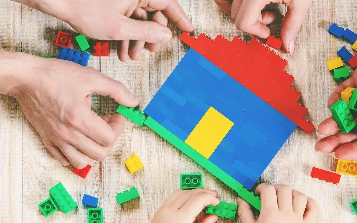 Close up of a parent and child's hands building a Lego house on the floor.