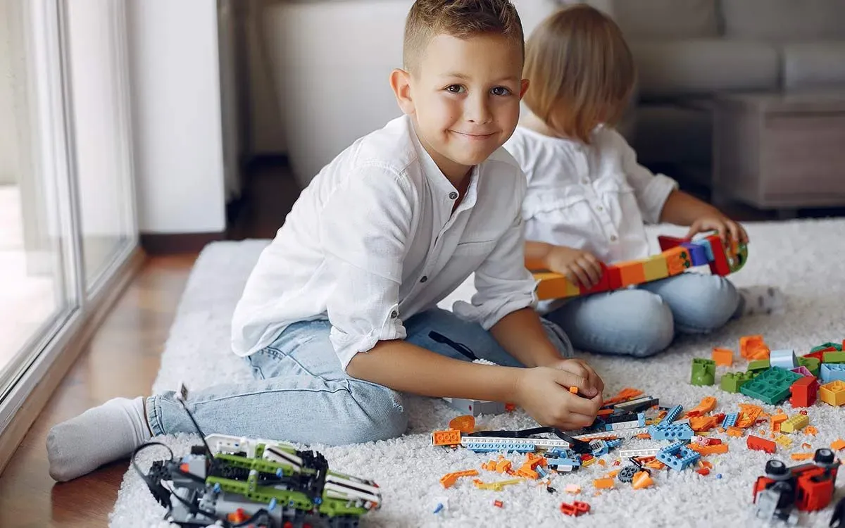 Boy smiling as he sits on the floor and plays with his Lego.