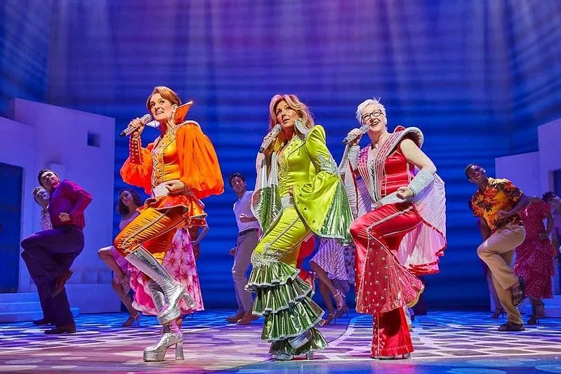 The cast of Mamma Mia performing a song wearing bright ABBA costumes.