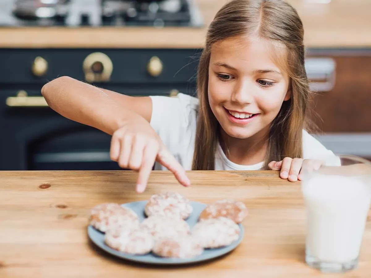 Girl smiling as she is about to take a cookie from the plate.