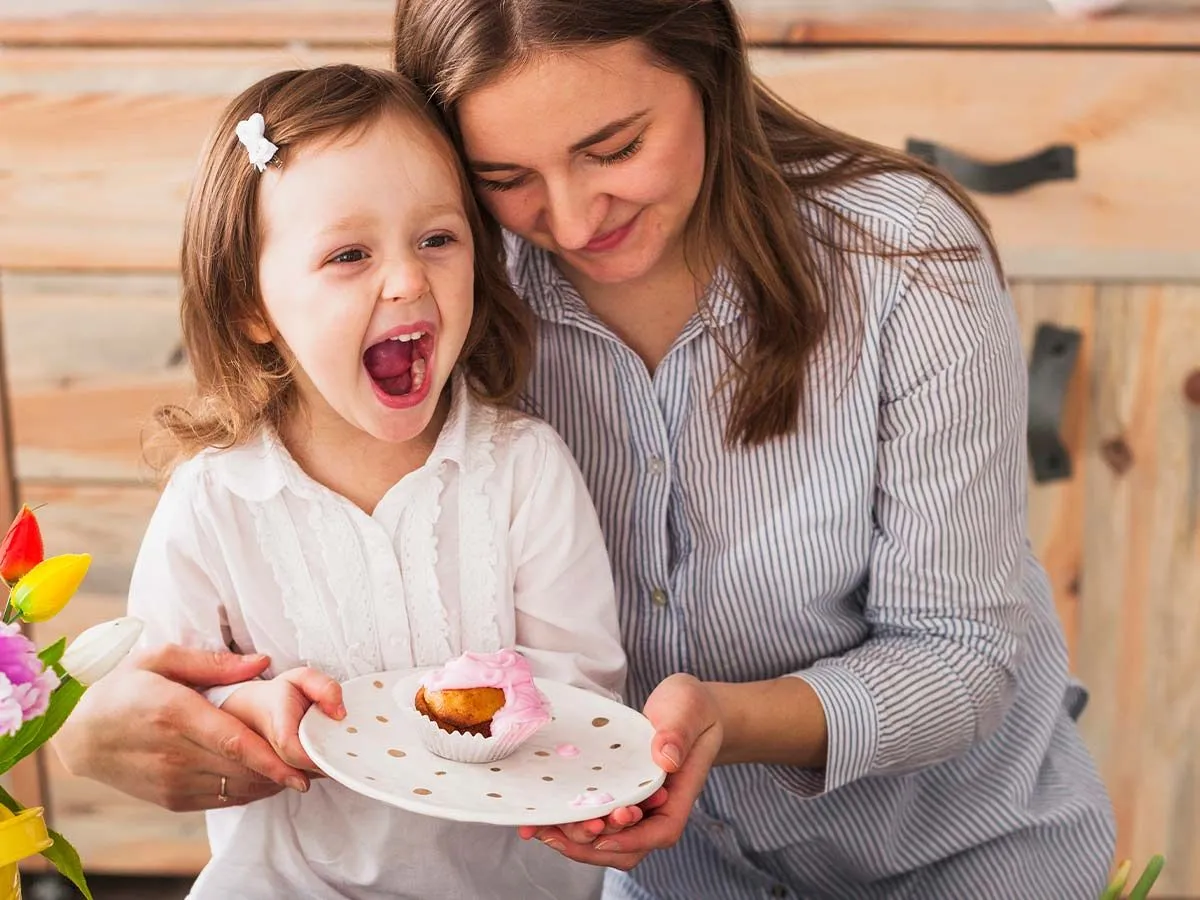Mum hugging her daughter who is holding a plate of cake and laughing at baking puns.