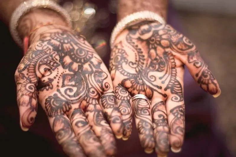 Two hands held out palms facing upwards to show off their intricate henna work.